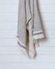 Beige and black Turkish waffle bath towel hanging against white wood wall