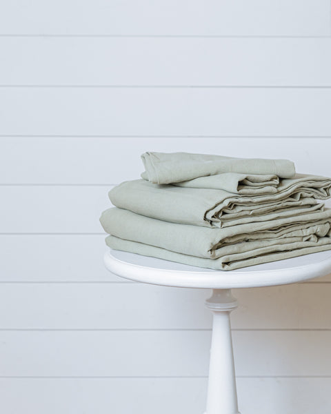 Sage green linen-cotton duvet cover set folded on bed with matching pillowcases