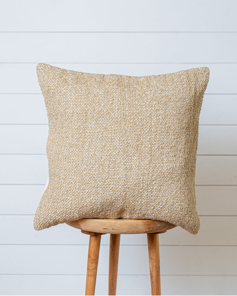 Textured sand-beige cotton cushion cover on wooden stool with white wall backdrop