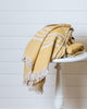 Mustard and ecru linen and Turkish cotton throw with fringe folded on wooden stool