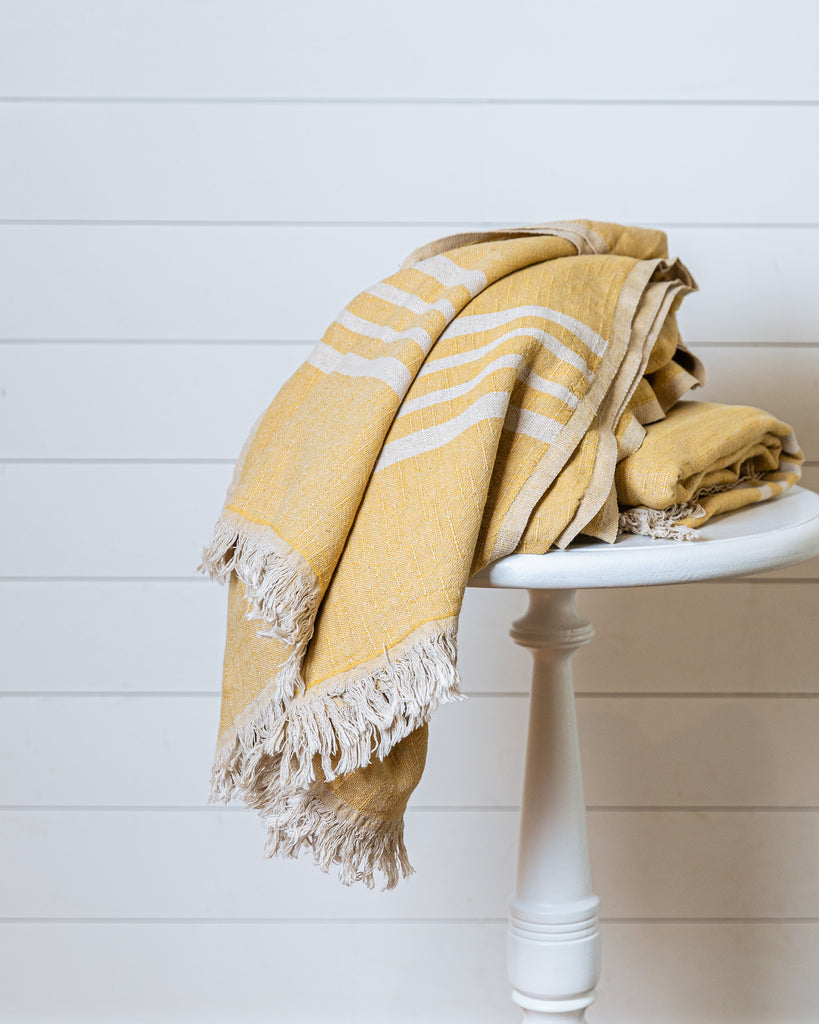 Mustard and ecru linen and Turkish cotton throw with fringe folded on wooden stool