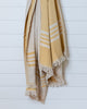 Mustard and ecru striped linen and Turkish cotton throw with fringe hanging on white wall
