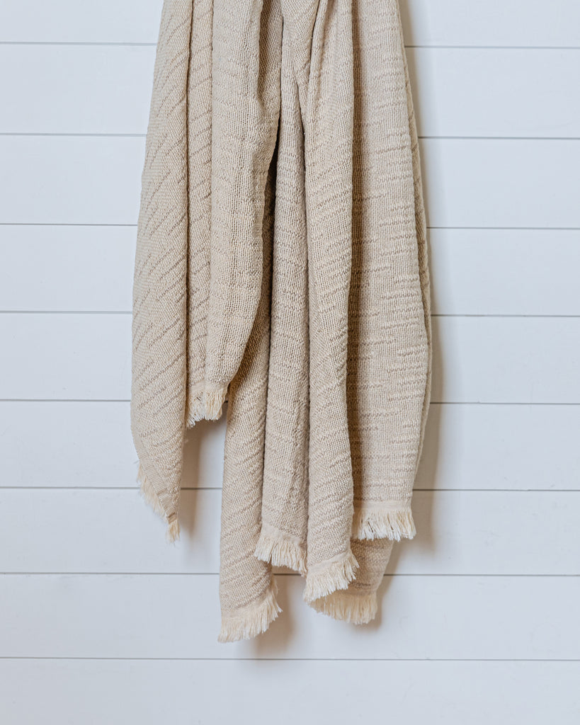 Sand-colored linen and Turkish cotton throw with textured weave hanging on white wall