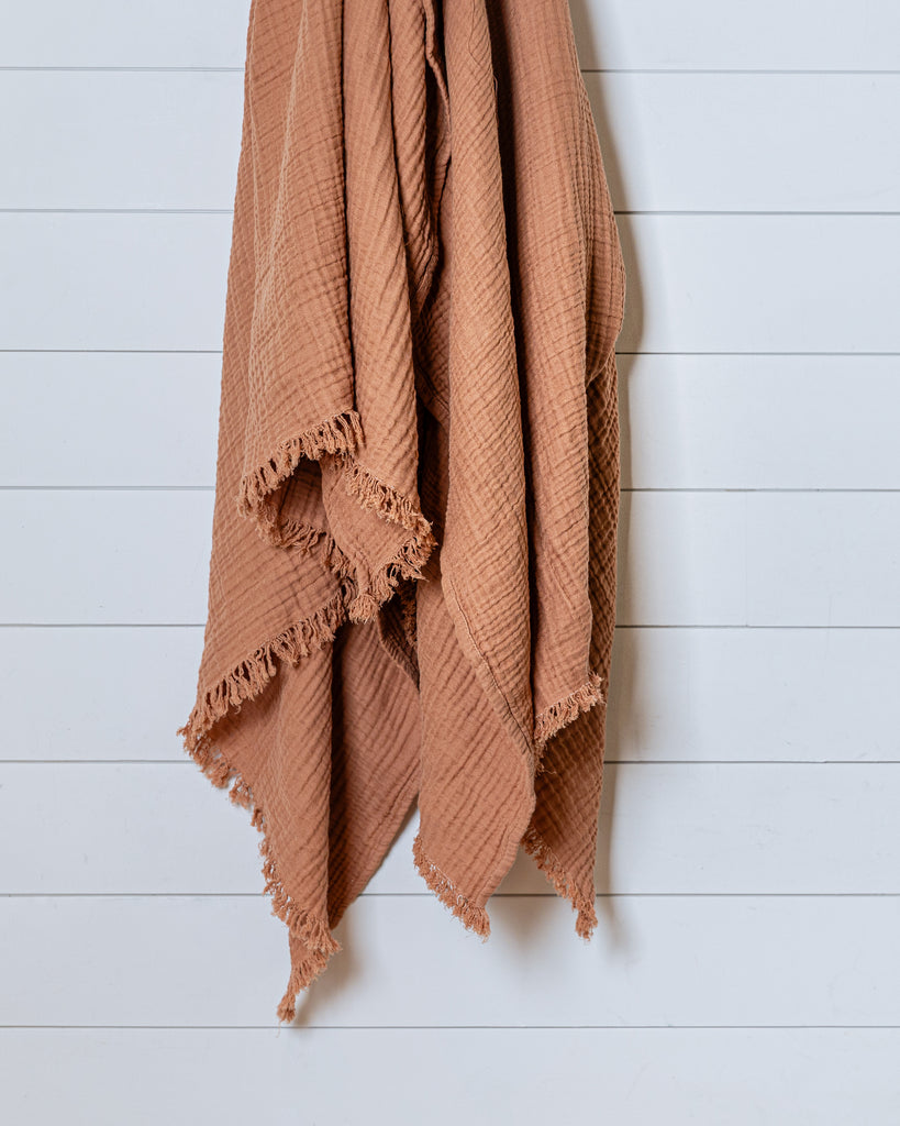 Cinnamon brown, cannelle muslin cotton throw with lightweight crinkled texture and fringed edges, hanging on wall