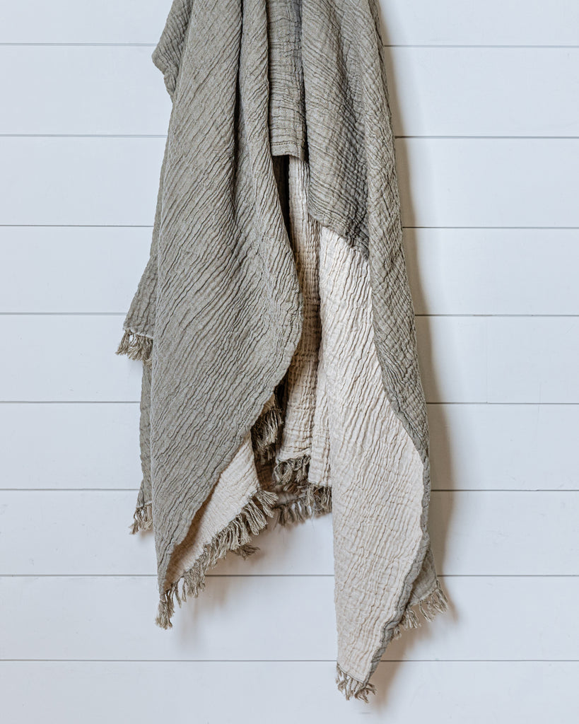 Reversible olive and ecru muslin cotton throw with soft crinkled texture and fringed edges hanging on wall