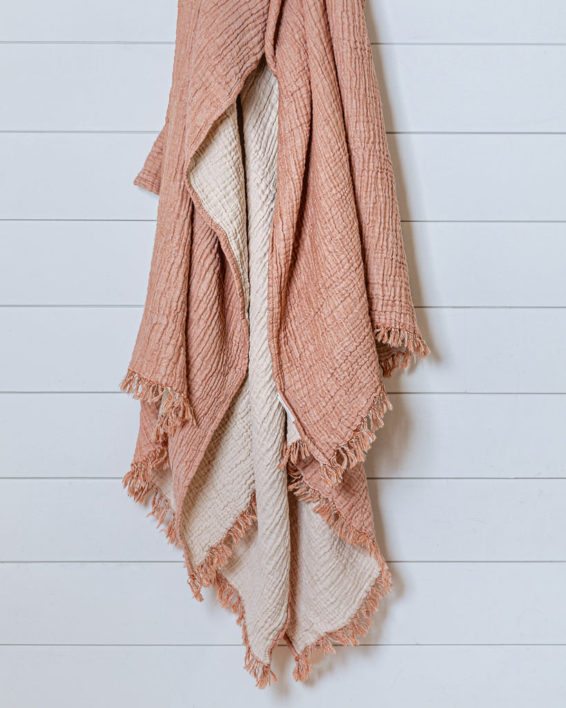 Terracotta and ecru muslin cotton throw with naturally crinkled texture and delicate fringes, hanging on white wall