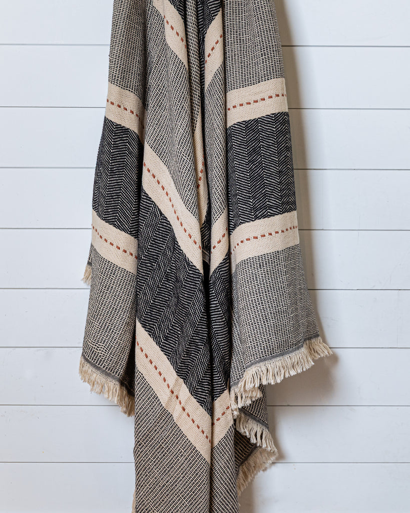 Black and sand woven cotton throw with terracotta accent hanging on white wall
