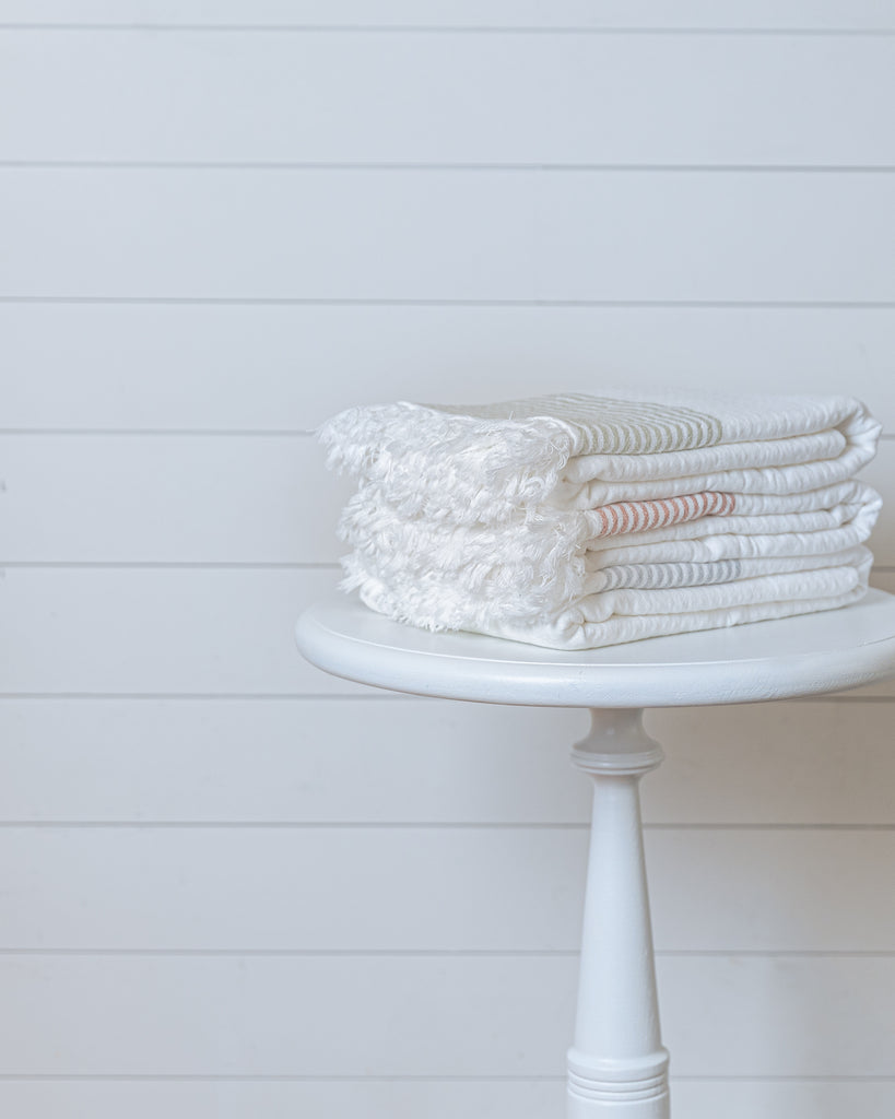 Stack of ivory Turkish cotton waffle bath towels with soft stripes on white stool