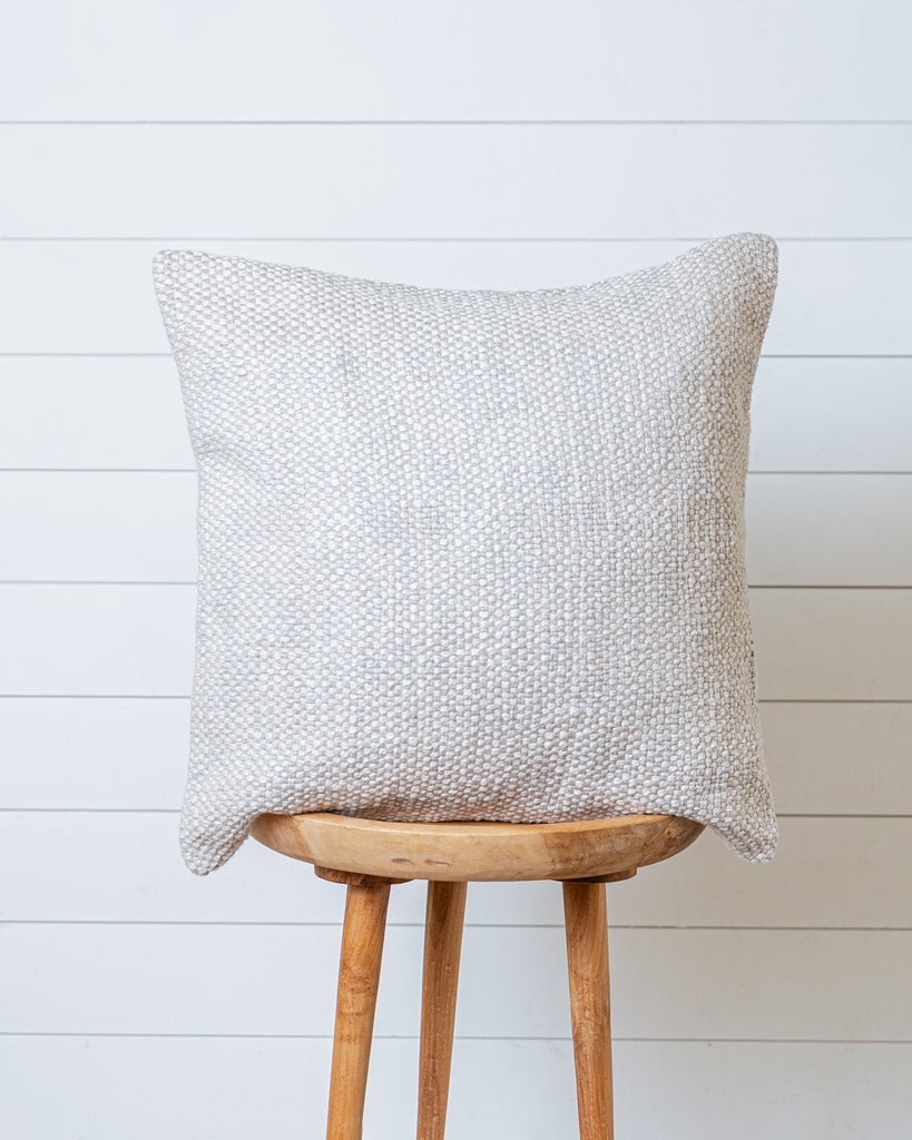 Light beige textured cotton cushion cover with linen and greige tones on wooden stool