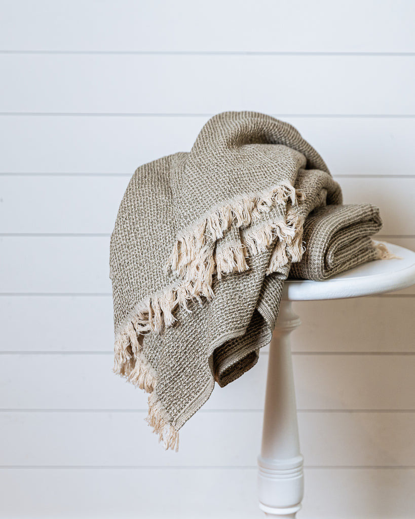 sage green waffle-knit cotton throw with tassel fringe draped over stool