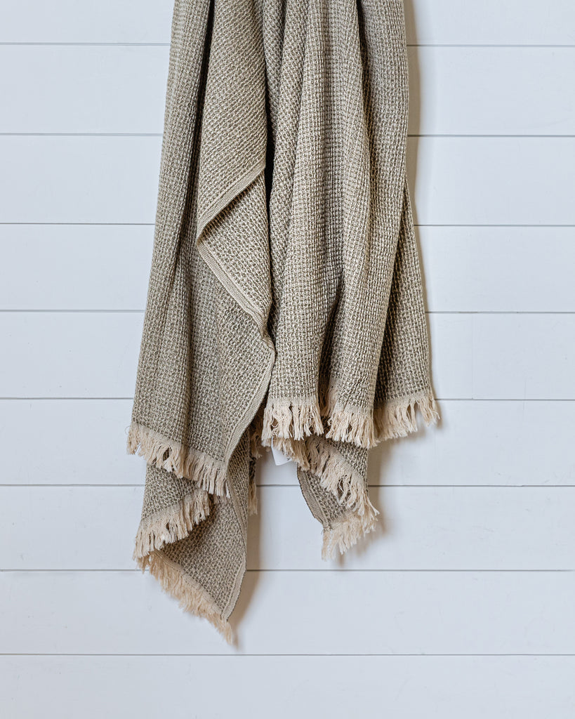 Sage green and sand waffle-knit Turkish cotton throw hanging on white wall