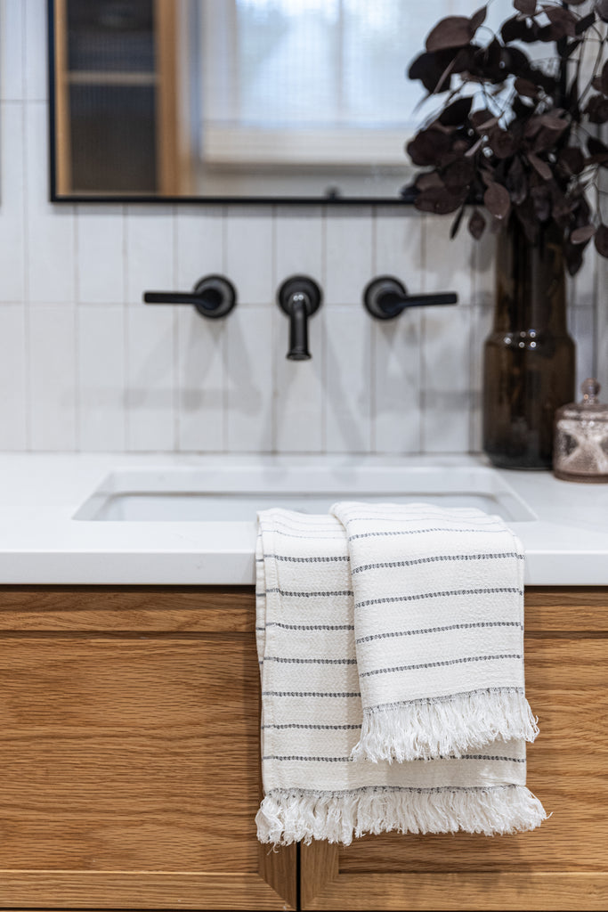 Folded off-white bamboo hand towels with subtle stripes on wooden bathroom cabinet