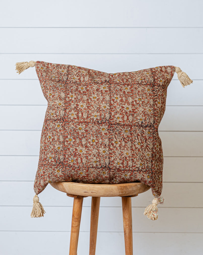 Terracotta and sand patterned cotton cushion cover with tassels on wooden stool