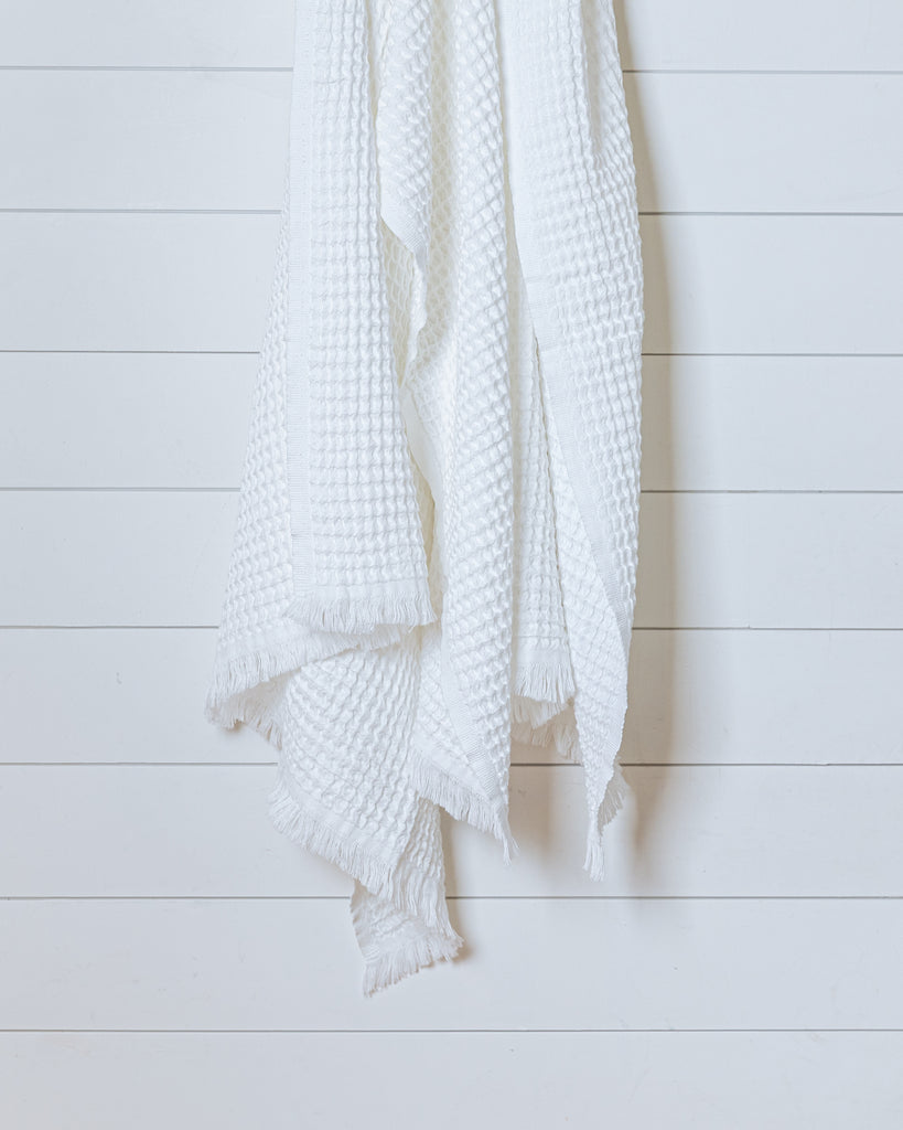 White Turkish waffle bath towel hanging on white wood panel wall