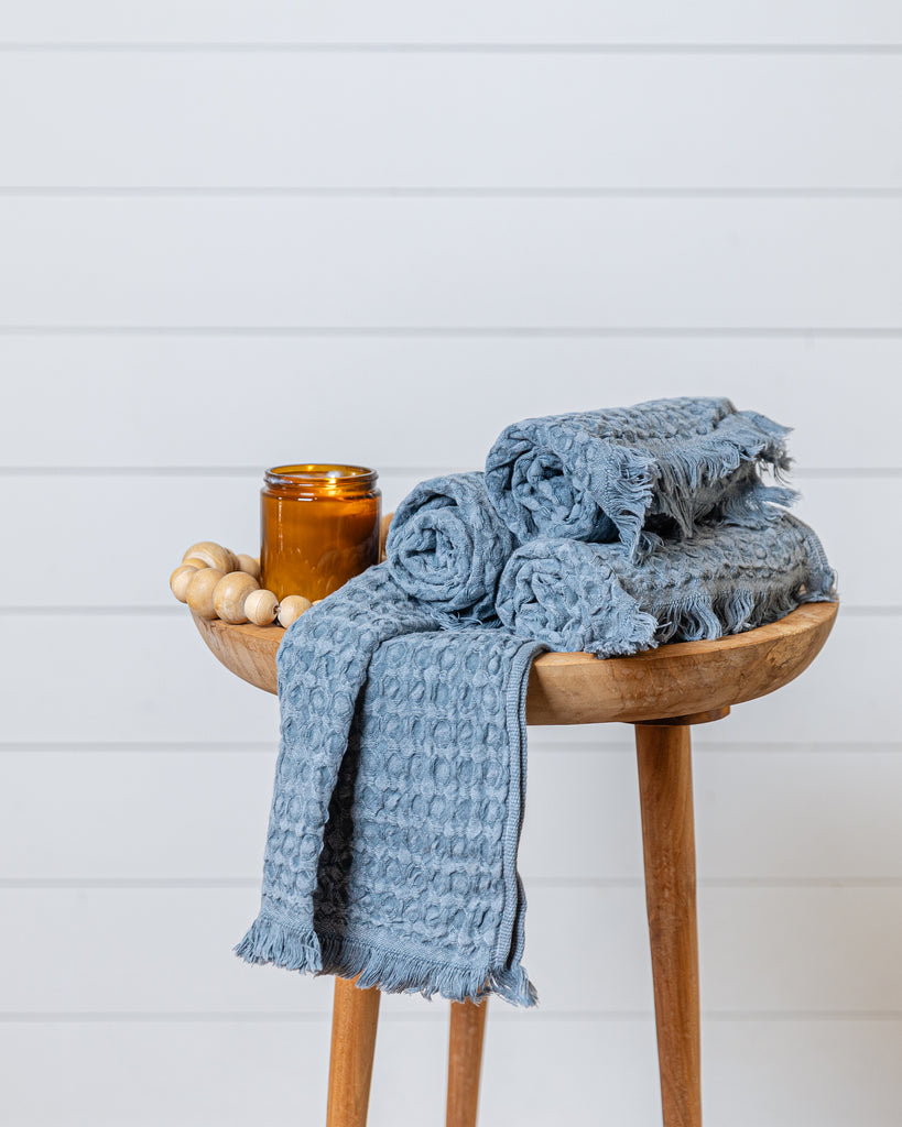 Slate blue waffle-knit cotton hand towel draped over wooden stool