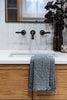 Slate blue waffle-knit cotton hand towel draped over white bathroom sink with wood cabinet