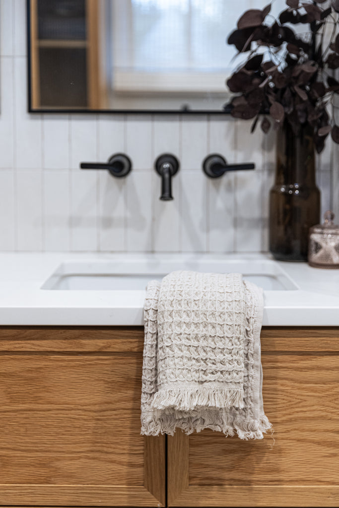 Neutral beige waffle cotton hand towel displayed over white sink and wood bathroom cabinet