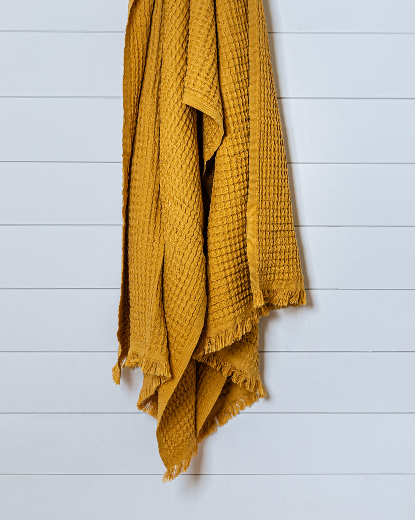 Mustard yellow Turkish waffle bath towel hanging on white wood panel wall