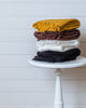 Stack of Turkish waffle bath towels in mustard, burgundy, white, and deep navy, folded on a stool