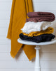 Stack of Turkish waffle bath towels in mustard, burgundy, white, and deep navy, folded on a stool