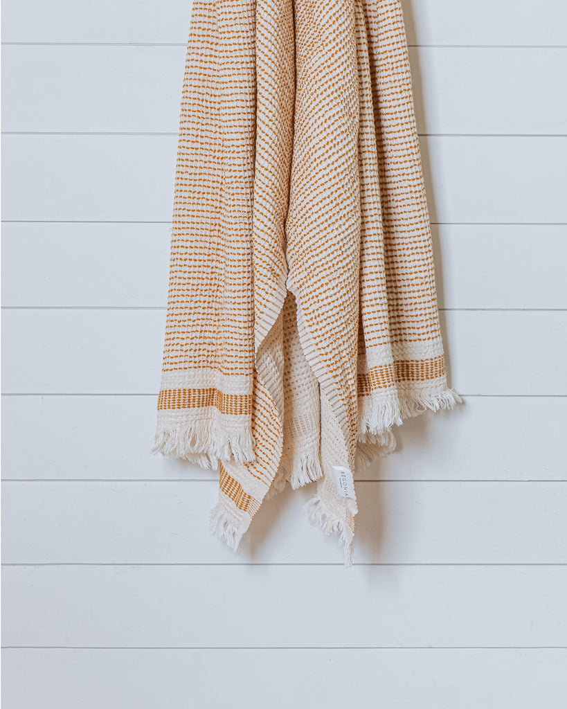 Beige and mustard yellow Turkish waffle bath towel displayed hanging against white wall
