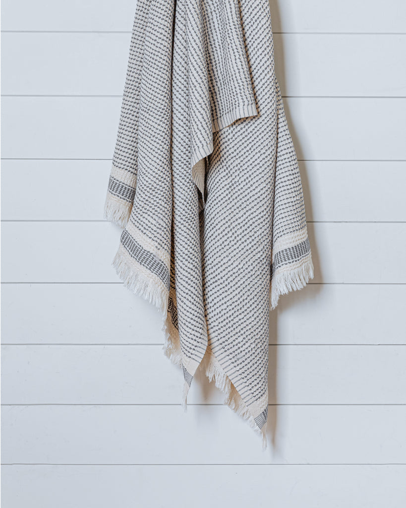 Beige and charcoal gray Turkish waffle bath towel hanging on white wood panel wall