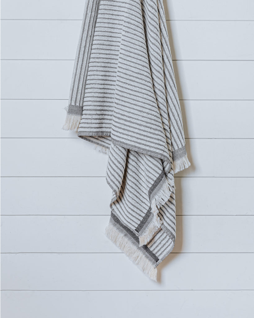 Ivory Turkish cotton bath towel with thin black stripes hanging on white wall