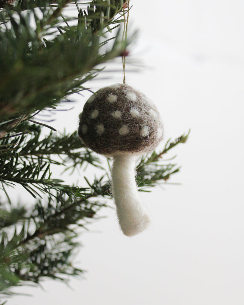 Handmade wool felt mushroom ornament in brown and cream on evergreen tree, artisan holiday decor